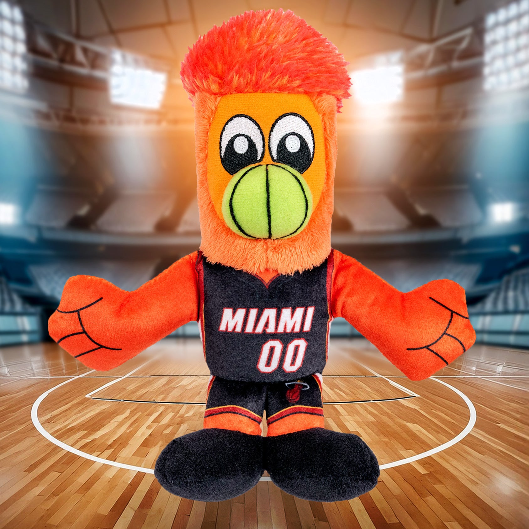 The Bleacher Creatures Miami HEAT Burnie Icon Chibi Plushie, with bright orange fur, a green beak, and a MIAMI 00 jersey, stands proudly on a hardwood basketball court inside a spacious, well-lit arena.