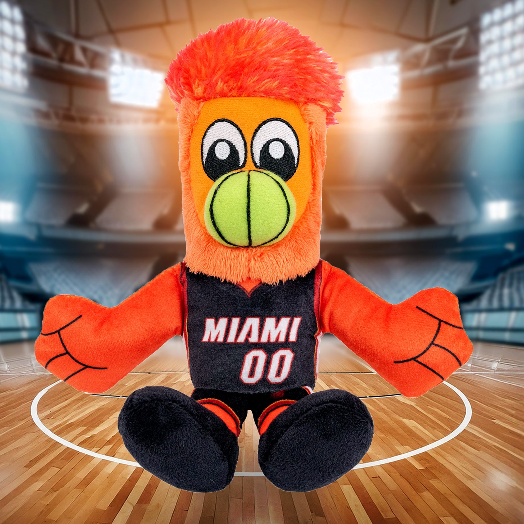 The Bleacher Creatures Miami HEAT Burnie Icon Chibi Plushie, featuring vibrant orange fur, a green beak, and a MIAMI 00 jersey, sits on a basketball court with an empty arena in the background.