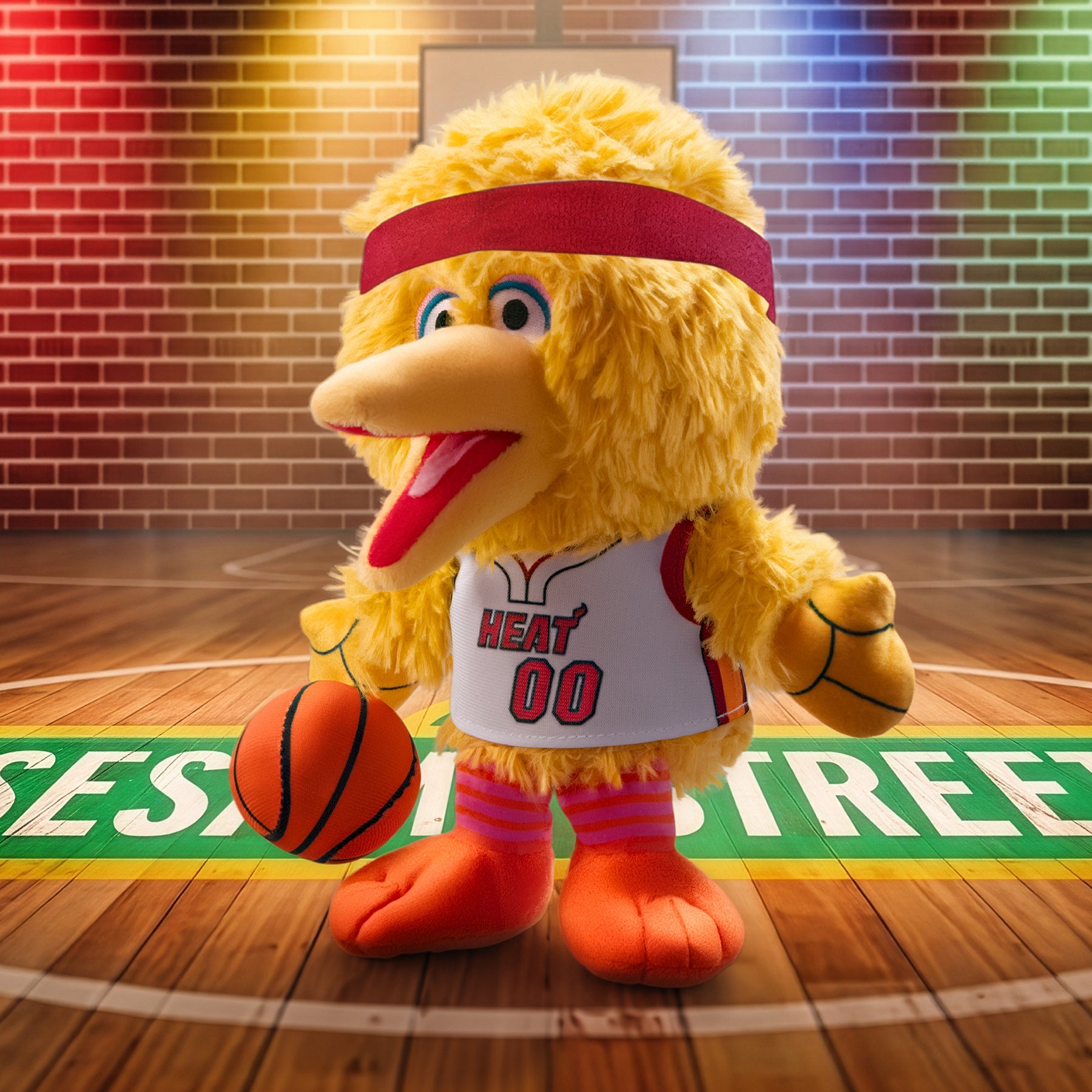 A Miami HEAT Big Bird Association Plushie by Bleacher Creatures stands on the court in a basketball jersey, holding a basketball, with SESAME STREET displayed on the floor and colorful lights illuminating the background.
