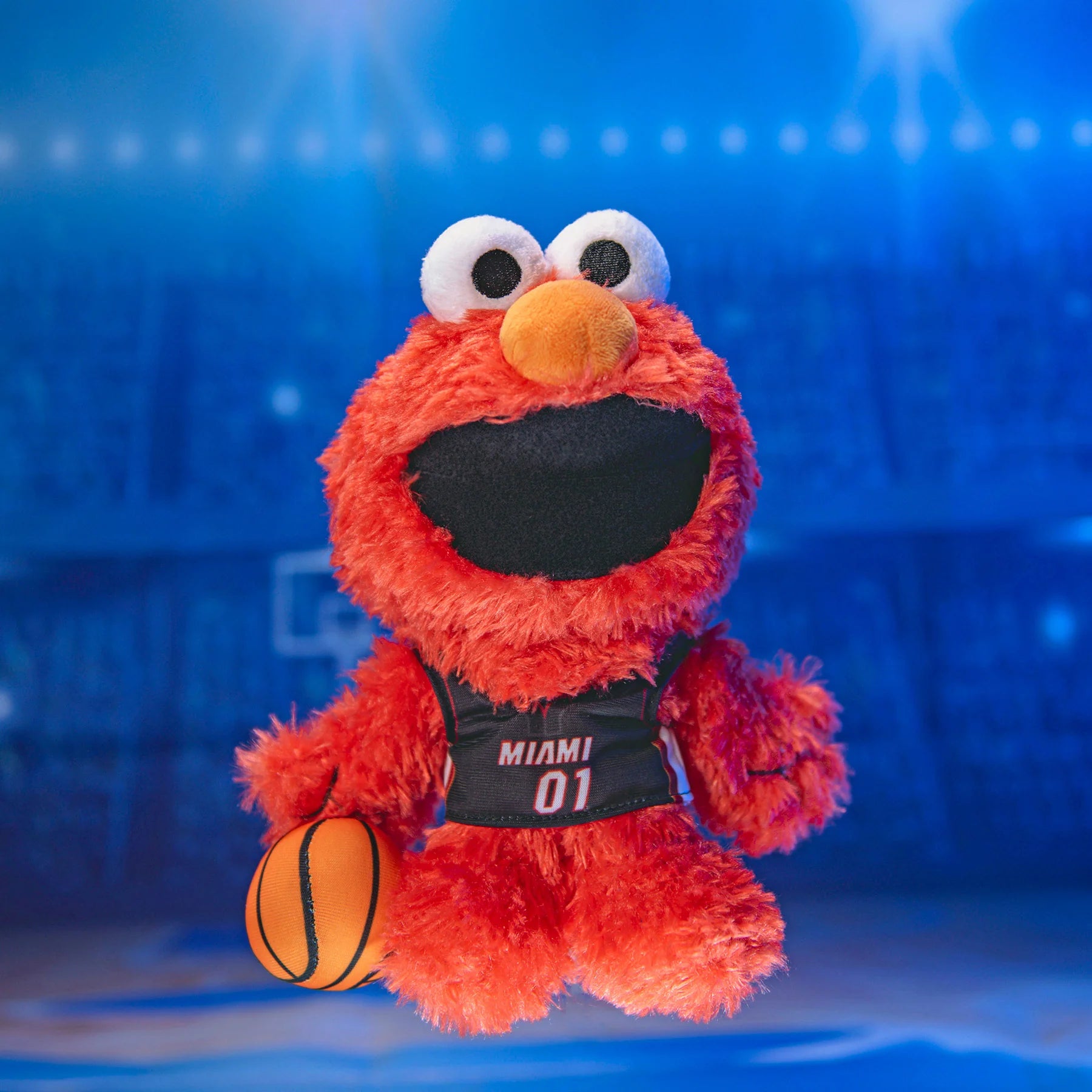 The Bleacher Creatures Miami HEAT Elmo Plush features Elmo in a black Miami 01 jersey holding a basketball on a blue-lit court—an adorable NBA x Sesame Street collectible.