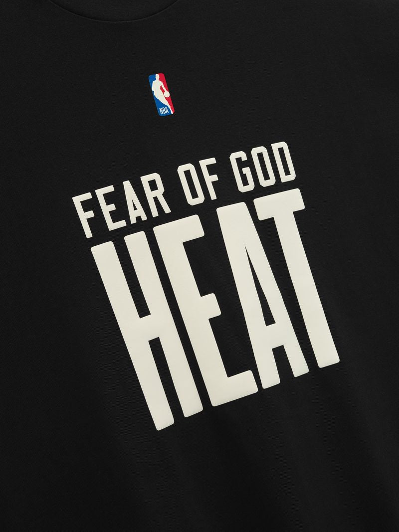 Close-up of the Fear Of God Essentials Miami HEAT Tee, a black cotton jersey shirt with the NBA logo and bold white HEAT lettering, inspired by classic ’90s oversized T-shirt style.