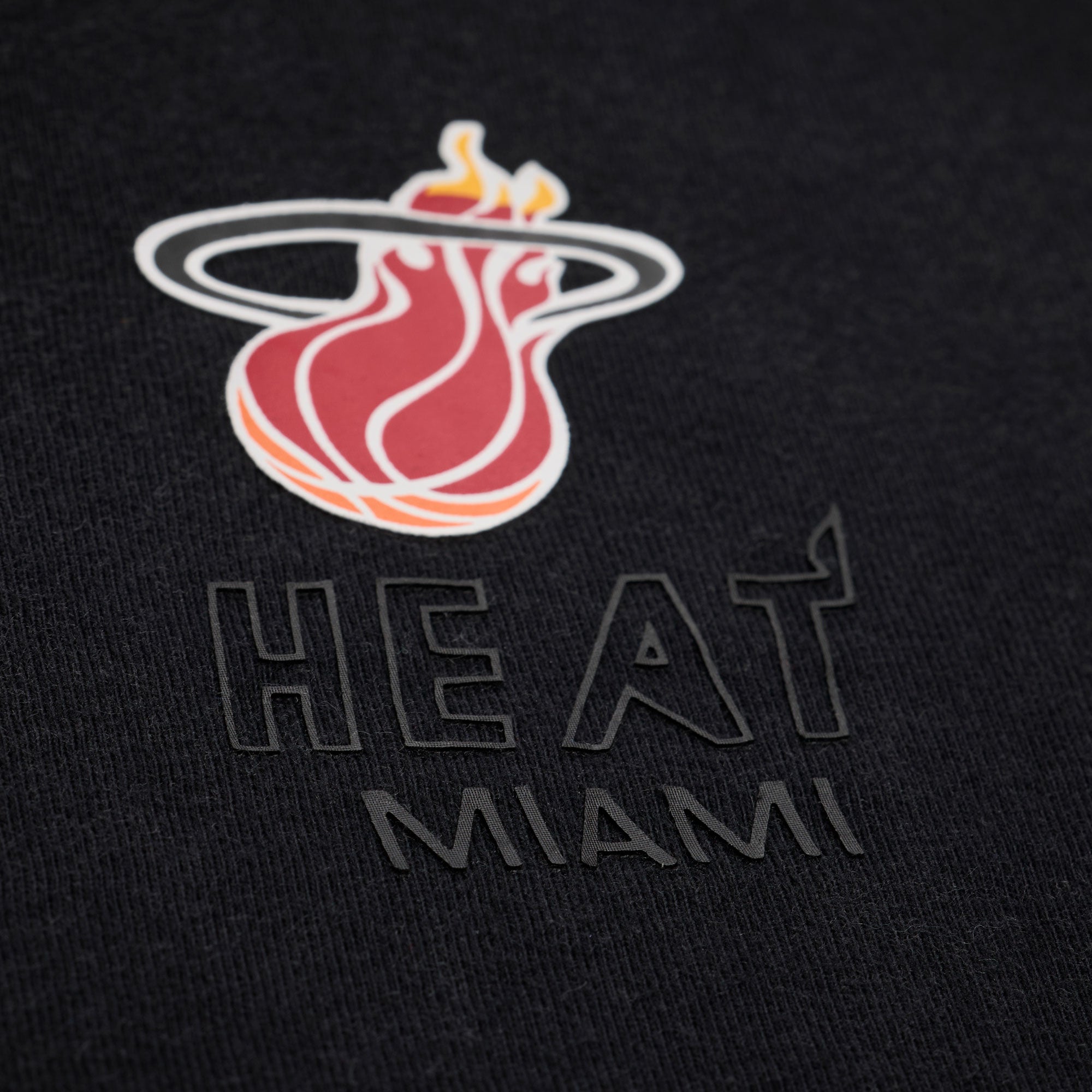 Close-up of the Mitchell & Ness Miami HEAT Core Logo Women’s Crop Tee—a black cotton cropped tee featuring the Miami Heat basketball team’s flaming basketball logo and “HEAT MIAMI” printed below, designed in a relaxed fit and easy to machine wash.