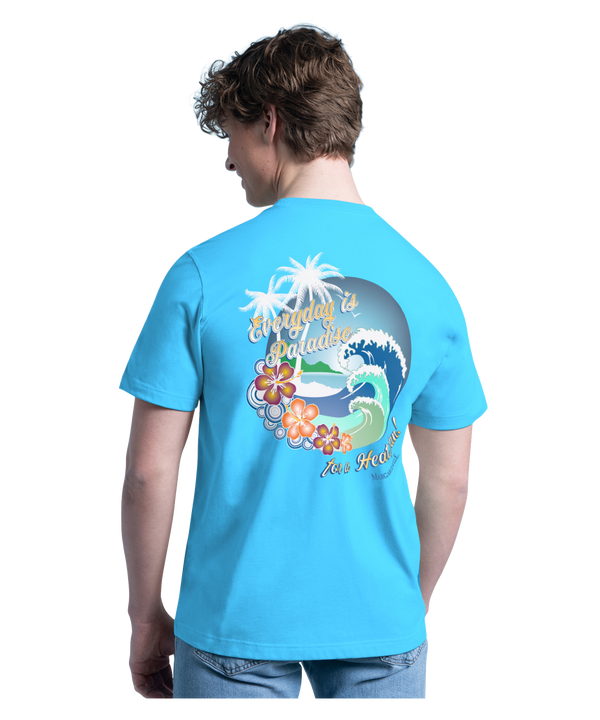 A smiling young man with curly hair wears the G-III Sports Margaritaville Miami HEAT 'Everyday is Paradise' Tee and light blue jeans, standing against a plain white background.