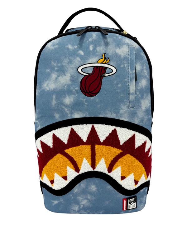 Introducing the Court Culture x Sprayground Miami HEAT Tie-Dye Jaw Backpack by Sprayground—a limited edition piece crafted from blue denim and showcasing an embroidered Miami Heat logo at the top, along with a bold shark mouth design over an orange basketball graphic on the front.