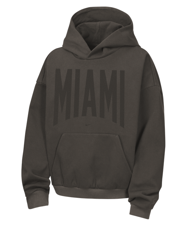 The Nike Miami HEAT Oversized Fleece Travel Youth Hoodie is a dark gray, loose-fit hoodie made from a soft cotton-polyester blend, featuring bold black “MIAMI” lettering across the chest and a convenient front kangaroo pocket.