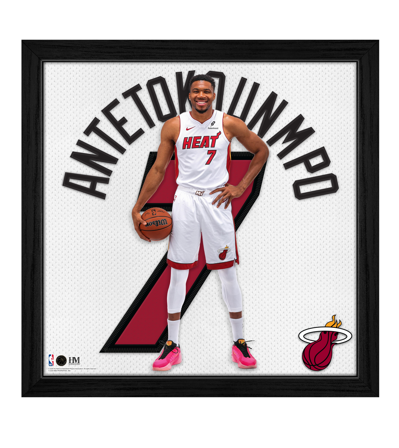 A basketball player in a Miami Heat uniform stands holding a ball, with Antetokounmpo and the number 7 behind him, and the Miami Heat logo in the corner. The Highland Mint Giannis Antetokounmpo Miami HEAT Impact Jersey Frame is an officially licensed, framed NBA art piece that captures an iconic moment for any fan.