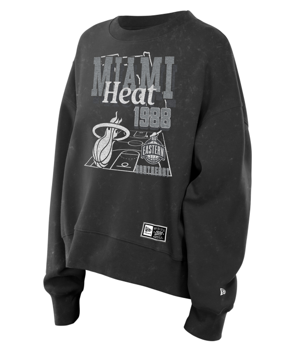 The New Era Miami HEAT Mineral Wash Women’s Crewneck is a black sweatshirt featuring MIAMI Heat 1988 text, basketball court graphics, and team logos on the front. Crafted from a soft cotton-polyester blend with a trendy cropped relaxed fit, this New Era crewneck is displayed on a plain white background.