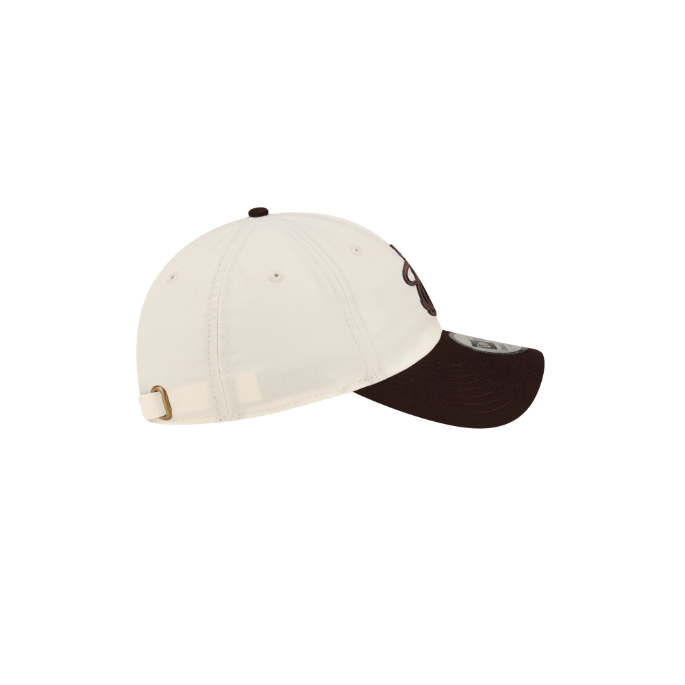 Court Culture x New Era Café y Leche Dad Cap: an off-white polyester baseball cap with a dark brown brim and button top, featuring an embroidered logo on the front and an adjustable metal buckle strap at the back.