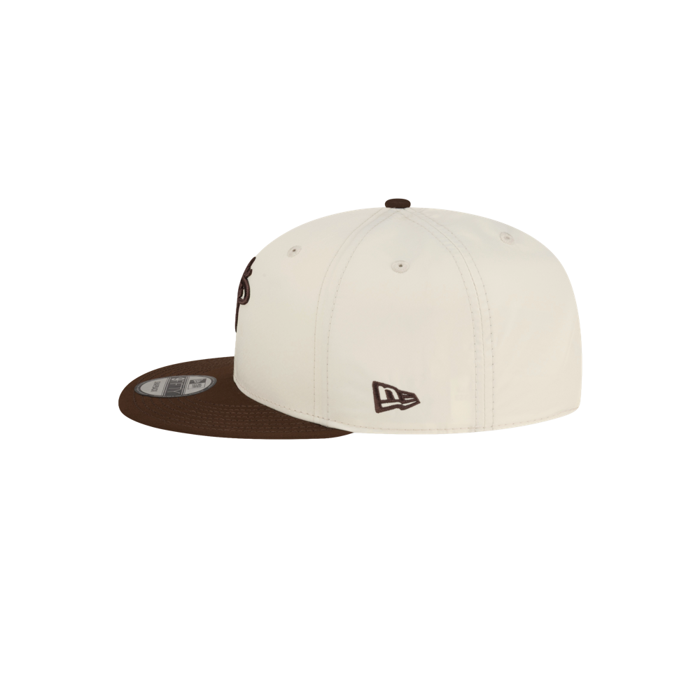 Cream polyester Court Culture x New Era Café y Leche snapback cap with a brown visor, featuring a brown logo on the side and a sticker on the brim.