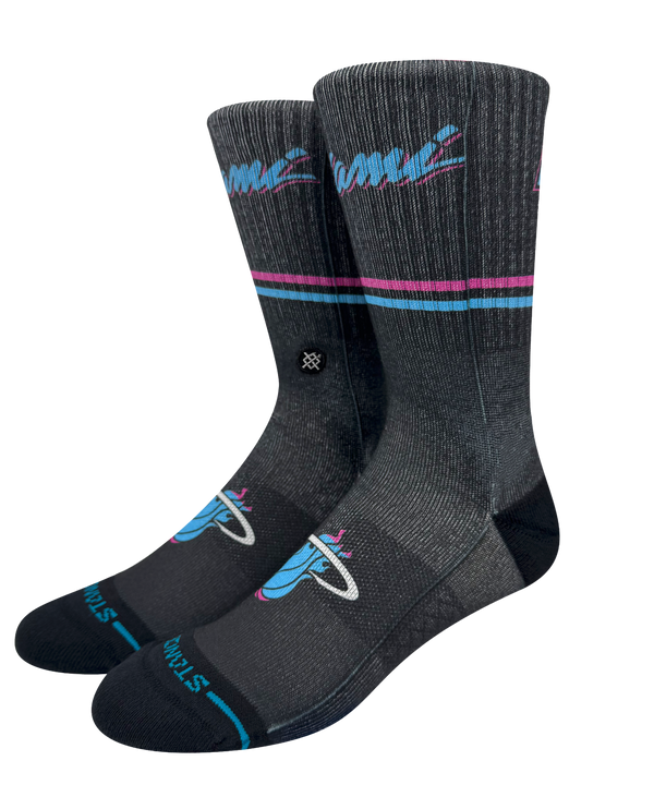 The Stance Miami HEAT Original Vice Nights Socks feature teal and pink stripes, a flaming basketball logo, and “Finals” near the toes. These dark gray crew socks have a ribbed texture and mid cushion, shown upright against a plain background.