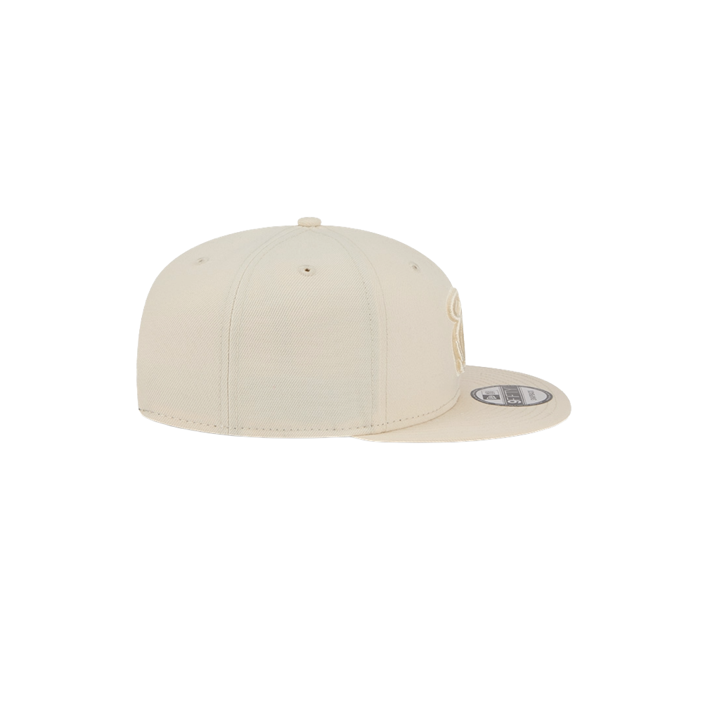 The New Era Miami HEAT Beige Color Pack Snapback is a beige polyester flat-brim cap with a sticker on the brim, minimal crown detail, and an adjustable fit. Shown from the side against a white background. One size fits most.