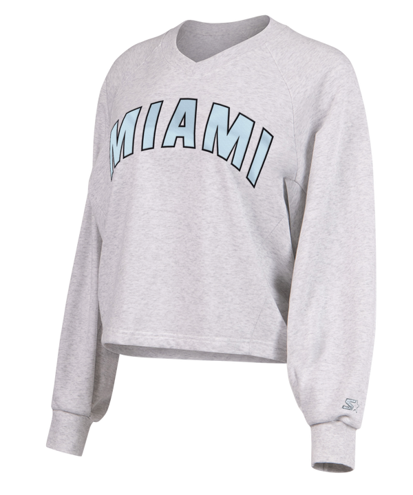 The G-III Miami HEAT Faceoff Women's Crewneck by G-III Sports is a light gray, relaxed-fit sweatshirt with MIAMI in large, light blue outlined letters across the chest. Features ribbed cuffs, crew neck, cotton-poly blend. Machine wash cold.